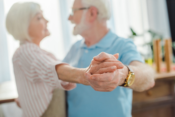Selective focus of senior couple holding hands while dancing in kitchen - Fotografie, Obrázek