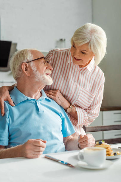 Selective focus of senior couple smiling at each other during breakfast in kitchen - Foto, imagen