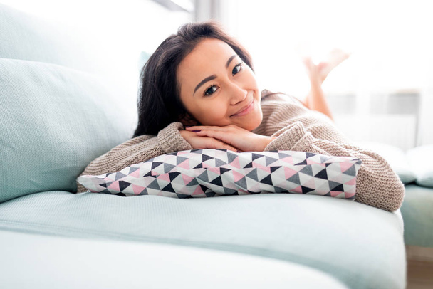 Happy asian girl lying on sofa with pillow at home - Foto, Imagem