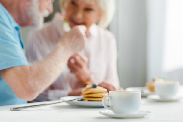 Enfoque selectivo de pareja mayor sonriéndose entre sí por café y panqueques en la mesa
 - Foto, Imagen