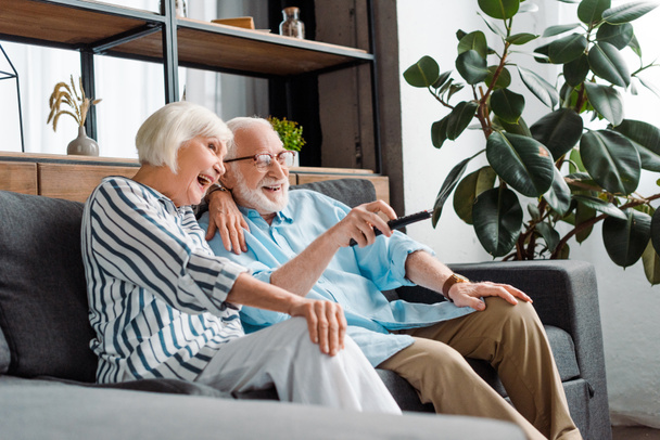 Selective focus of cheerful senior couple watching tv on couch in living room - Photo, Image