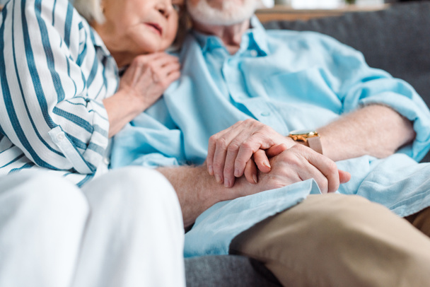 Selective focus of elderly couple holding hands while sitting on couch  - Zdjęcie, obraz