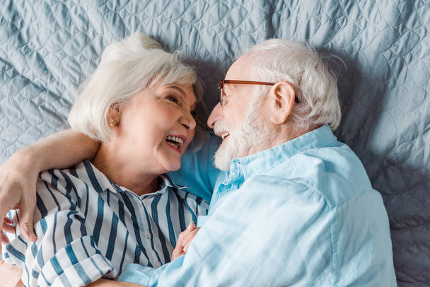 Top view of smiling senior couple smiling while lying on bed - Zdjęcie, obraz
