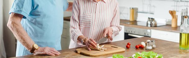 Vista recortada del hombre mayor de pie por la esposa cortando setas en la cocina, plano panorámico
 - Foto, imagen
