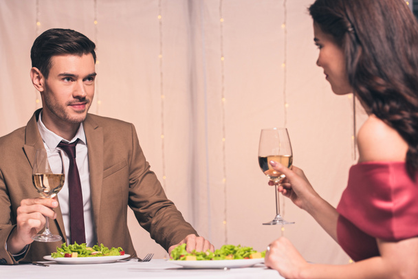 happy, elegant man and woman sitting at served table and holding glassed of white wine - Photo, image