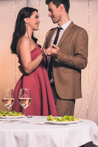 boldog, elegáns férfi és nő mosolyognak egymásra, miközben táncolnak az étteremben - Fotó, kép