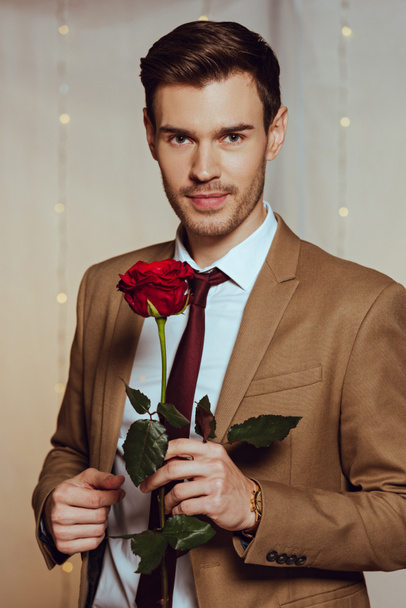 handsome, elegant man holding red rose while standing in restaurant and looking at camera - Fotografie, Obrázek