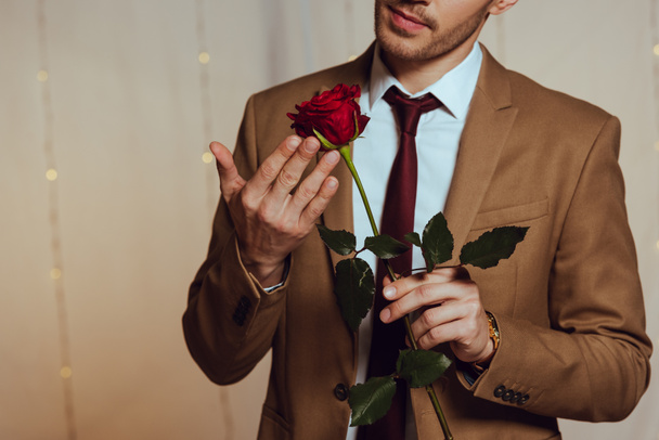 částečný pohled na elegantního muže držícího rudou růži při stání v restauraci - Fotografie, Obrázek