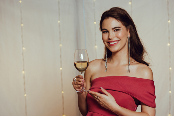 happy, elegant girl smiling at camera while holding glass of white wine in restaurant - Foto, afbeelding