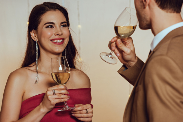selektivní zaměření atraktivní, šťastná dívka při pohledu na přítele při držení sklenice bílého vína - Fotografie, Obrázek