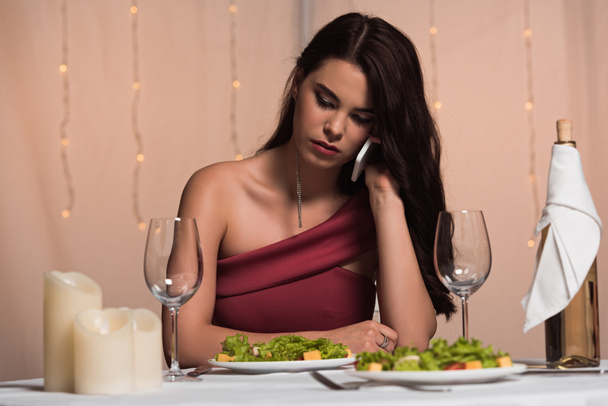 disappointed, elegant girl sitting at served table in restaurant and talking on smartphone - Photo, Image