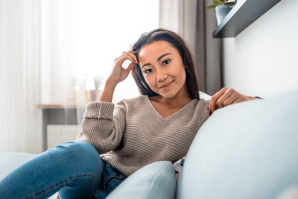 Relaxed smiling asian woman sitting on sofa at home - Foto, Imagem