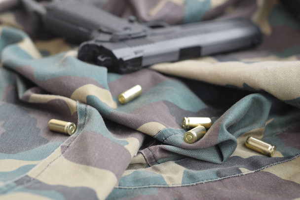 Les balles de 9mm et le pistolet reposent sur un tissu vert camouflage plié. Un set de tir ou un kit d'auto-défense
 - Photo, image