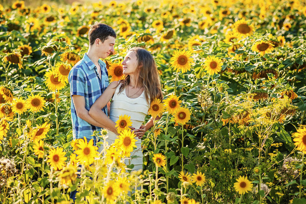 Young couple man and woman girlfriend and boyfriend wife and husband standing in sunflowers field looking at each other. Love, romance, togetherness, trust. Happy marriage. Sunflower in summer - Foto, afbeelding
