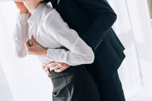 abgeschnittene Ansicht von Geschäftsmann im Anzug umarmt Sekretärin im Büro  - Foto, Bild