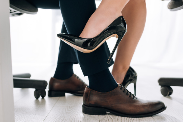 cropped view of secretary in heels touching leg of businessman in office  - 写真・画像