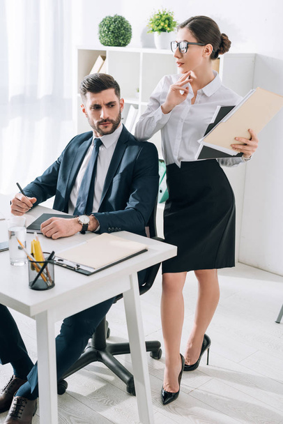 attractive secretary with folder touching shoulder of businessman in office  - Foto, immagini