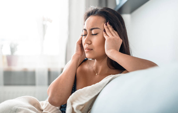 Verärgert depressives asiatisches Mädchen auf Couch leidet unter Kopfschmerzen Migräne - Foto, Bild