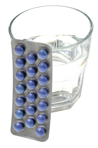 Blisterverpakking met geneesmiddelen geplaatst tegen een glas water close-up op een witte achtergrond - Foto, afbeelding
