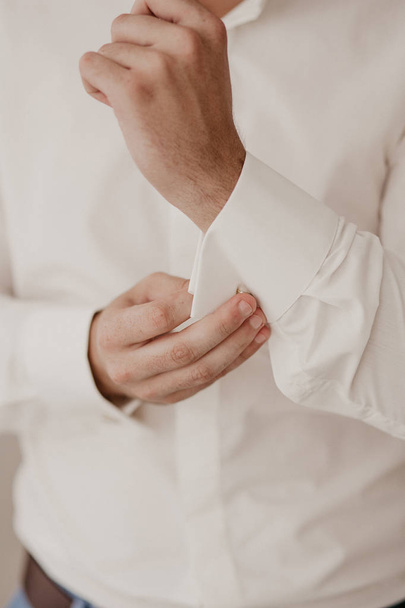 Mani in alto con i bottoni sulla camicia. Il processo di fissaggio dei bottoni sulla camicia bianca. Vista da vicino. Bottoni da sposo sui polsini della camicia. Mattina dello sposo
 - Foto, immagini