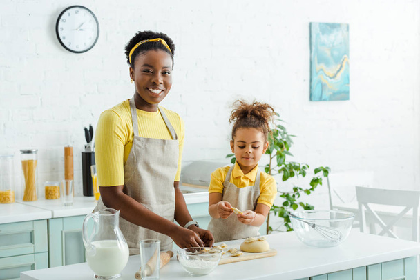 cheerful african american mother and cute kid in aprons sculpting dumplings  - 写真・画像