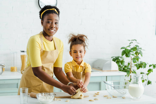 Αφροαμερικανή μητέρα κοντά σε χαρούμενο παιδί που σμιλεύει ζυμαρικά στην κουζίνα  - Φωτογραφία, εικόνα