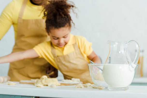 selective focus of jug with milk near bowl and cute african american kid sculping dumplings near mother  - Foto, immagini