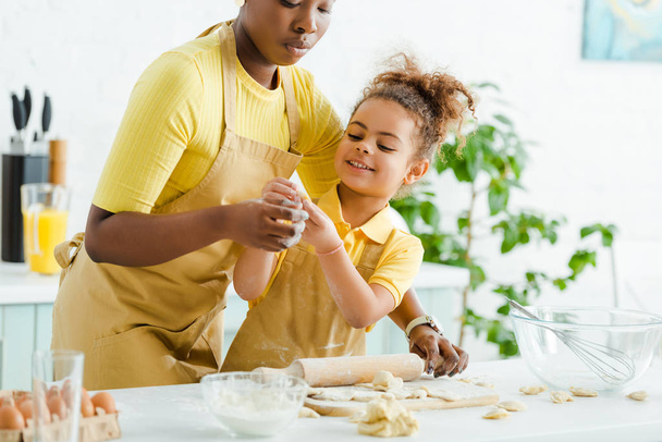 enfoque selectivo de niño afroamericano lindo sosteniendo masa cruda cerca de la madre y albóndigas en la tabla de cortar
  - Foto, imagen