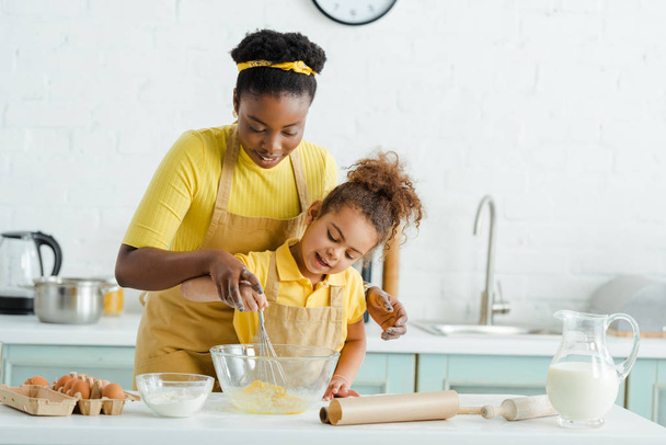 carino africano americano bambino guardando ciotola vicino allegra madre in cucina
  - Foto, immagini