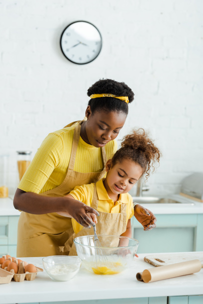 söpö afrikkalainen amerikkalainen lapsi ja onnellinen äiti tilalla vispilä lähellä kulhoa ruoanlaitossa keittiössä
  - Valokuva, kuva