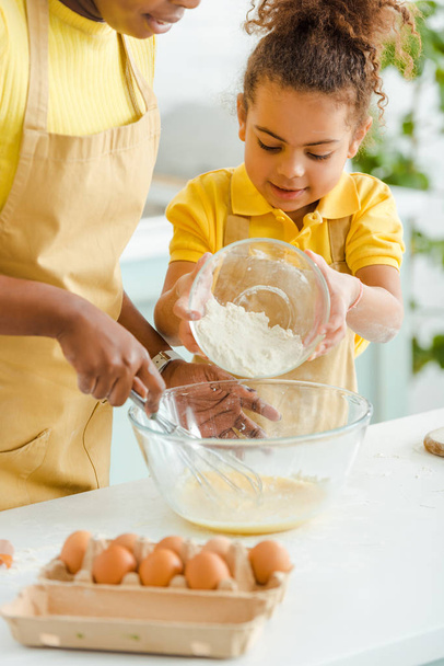 selective focus of cute african american kid holding bowl with flour near mother in kitchen  - Photo, Image