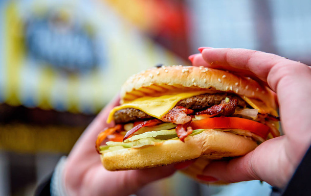 Woman hand is holding a fresh burger before eating on street - Valokuva, kuva