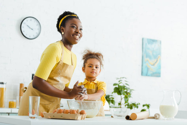 african american kid and cheerful mother smiling while cooking in kitchen  - 写真・画像