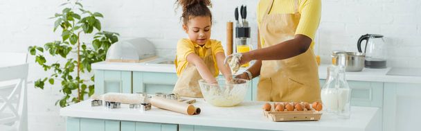 panoramic shot of african american mother and daughter kneading dough in kitchen  - 写真・画像