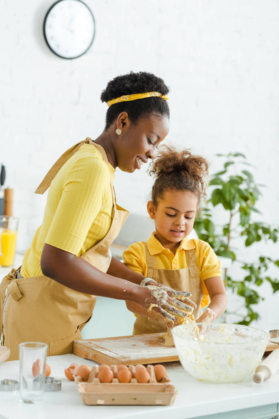cheerful african american mother and daughter kneading dough on cutting board  - Фото, зображення