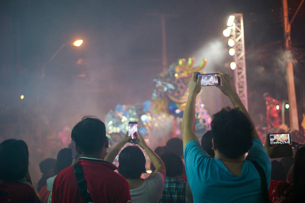 Selektiver Fokus auf die Hände hält das Mobiltelefon und zeichnet den Clip der Show mit Bewegungsunschärfe tanzenden Drachen im Hintergrund auf - Foto, Bild