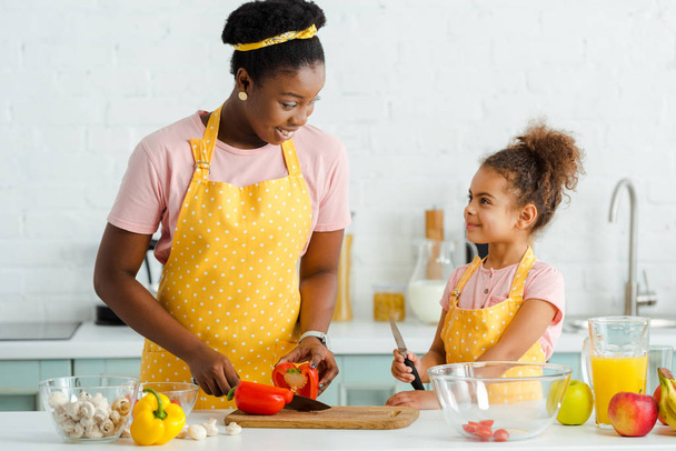 happy african american woman cutting bell pepper on cutting board near cute daughter  - Photo, Image