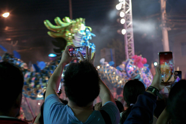Вибірковий фокус на руках тримає мобільний телефон і записує кліп шоу з розмитим рухом танцюючого дракона продуктивність у фоновому режимі
 - Фото, зображення