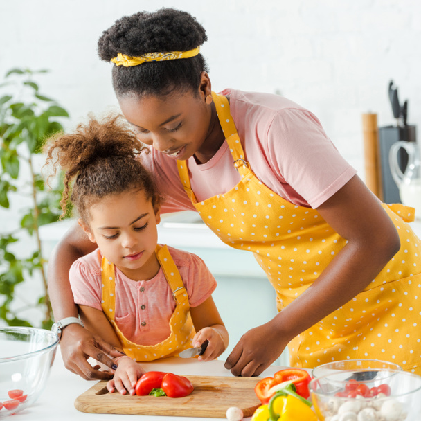 happy african american mother cutting bell pepper with cute daughter  - 写真・画像