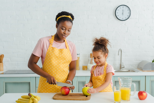attractive african american mother cutting apple near cute daughter  - Foto, Imagem