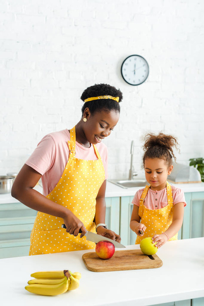 Χαρούμενη Αφροαμερικανή μητέρα και χαριτωμένη κόρη που κόβει μήλα.  - Φωτογραφία, εικόνα