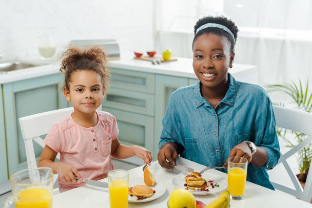 afro americano madre e figlia in possesso di posate vicino gustosi pancake su piatti
  - Foto, immagini