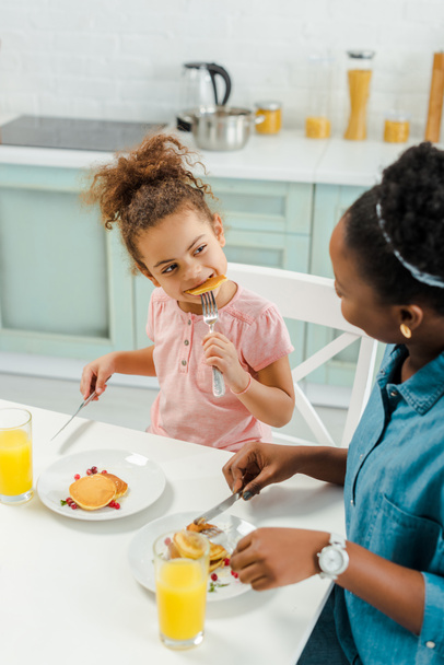 african american mother looking at daughter eating tasty pancakes  - Photo, Image