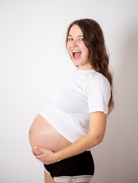 The young beautiful pregnant woman experiences strong emotions on a white background - 写真・画像