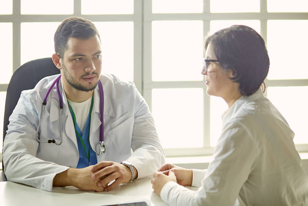 Joven médico hablando con un paciente en el consultorio
 - Foto, Imagen