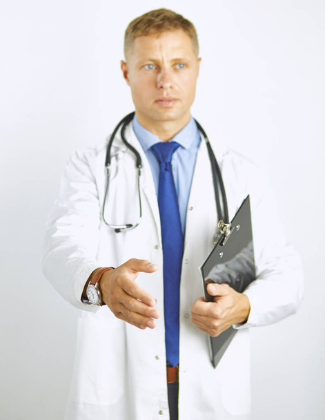 Young doctor in white coat with a stethoscope greets holding out his hand - Фото, изображение