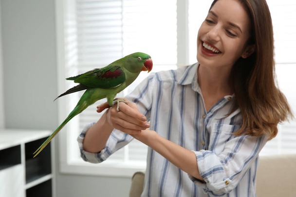 Young woman with cute Alexandrine parakeet indoors - Foto, imagen