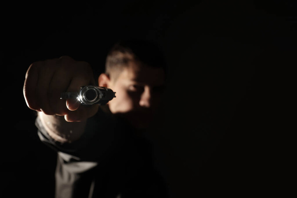 Professional killer on black background, focus on gun - Foto, Imagem