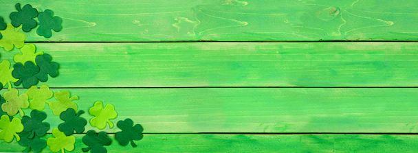Πανό ημέρας του Αγίου Πατρικίου με γωνιακό περίγραμμα από τριφύλλια. Πάνω άποψη πάνω από ένα πράσινο φόντο ξύλο. Αντιγραφή χώρου. - Φωτογραφία, εικόνα