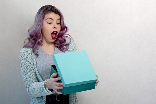 Shocked linda chica sosteniendo regalo en un fondo gris
 - Foto, imagen